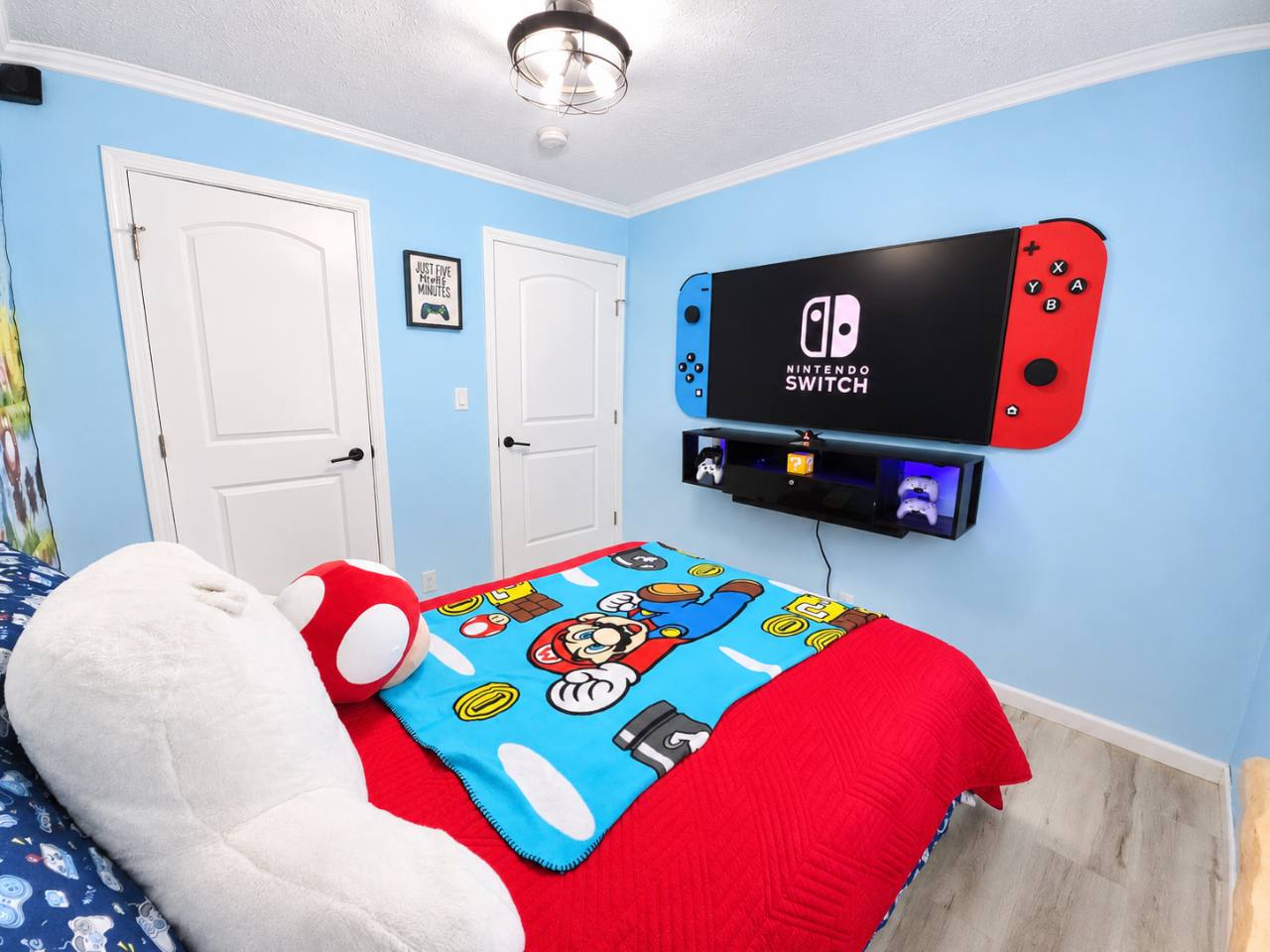 Mario-themed bedroom with blue walls, red bedding and a television framed by oversized Nintendo Switch controller decorations