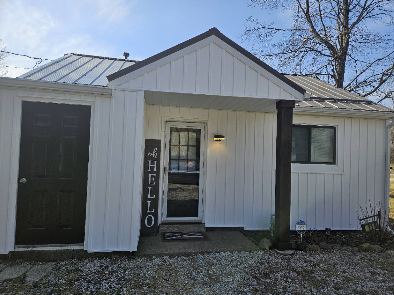 The White House of Green front exterior with white siding, dark trim, covered entrance and tall hello sign